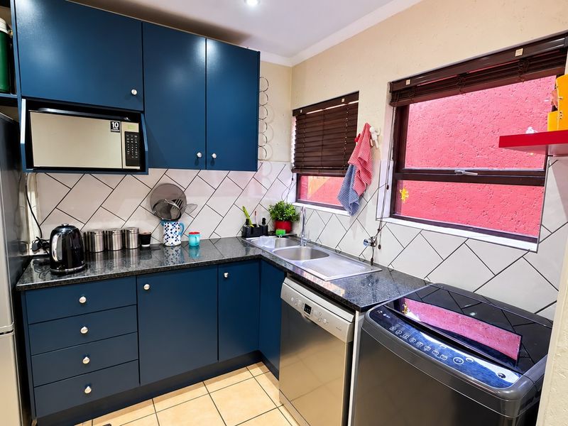 A functional kitchen featuring dark blue cabinetry, granite countertops, a double basin sink, and a tiled backsplash with integrated appliance space.