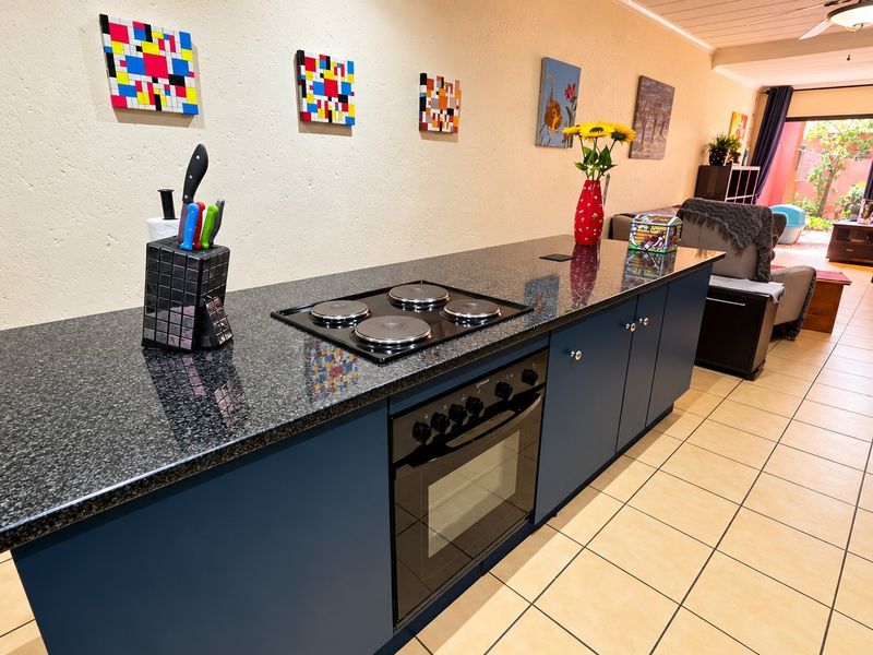 Open-plan living area featuring a kitchen island with granite countertops, built-in electric hob and oven, tiled flooring, and direct access to the patio.