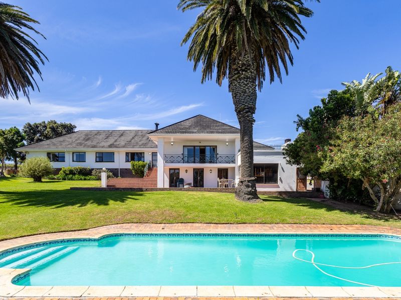 Rear view of the farm property featuring a swimming pool, expansive lawn, mature palm trees, and a two-story building with a balcony.