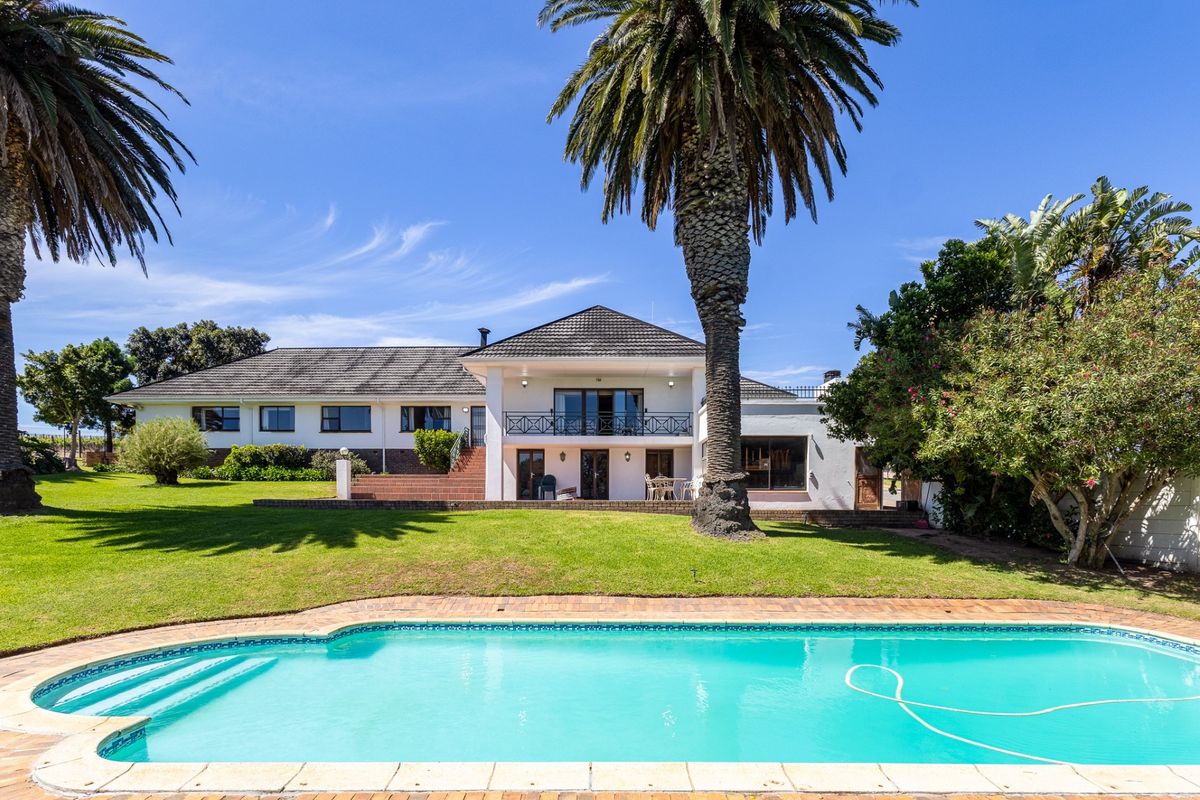 Rear view of the farm property featuring a swimming pool, expansive lawn, mature palm trees, and a two-story building with a balcony.