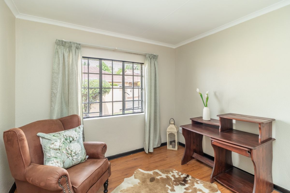 A well-maintained bedroom featuring laminate flooring, neutral wall tones, and a window fitted with security bars, offering a bright and functional living space.