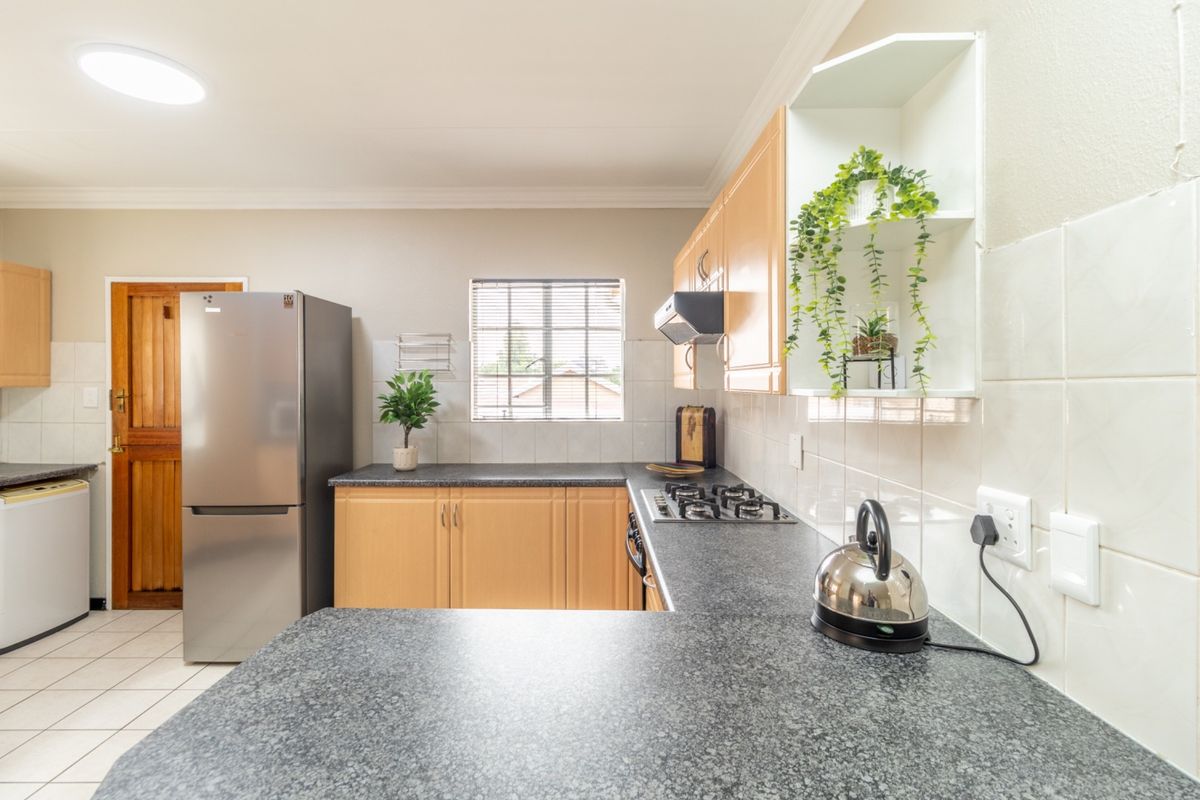 Functional kitchen featuring granite countertops, gas hob, extractor fan, and ample cabinetry with a tiled backsplash and flooring.