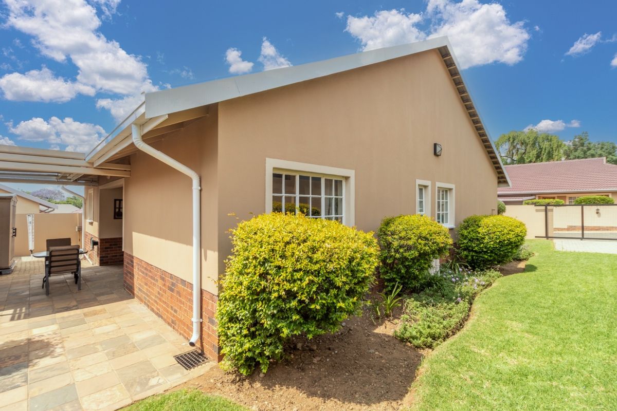 A well-maintained rear exterior view featuring a paved patio area, brick plinth detailing, and a neat landscaped garden.