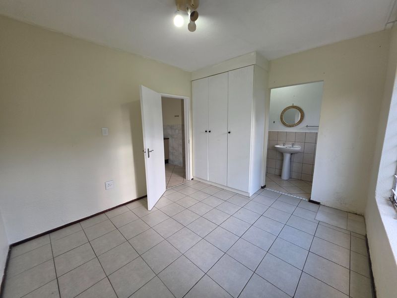 A spacious bedroom featuring built-in cupboards, tiled flooring, and an en-suite area with a pedestal basin.