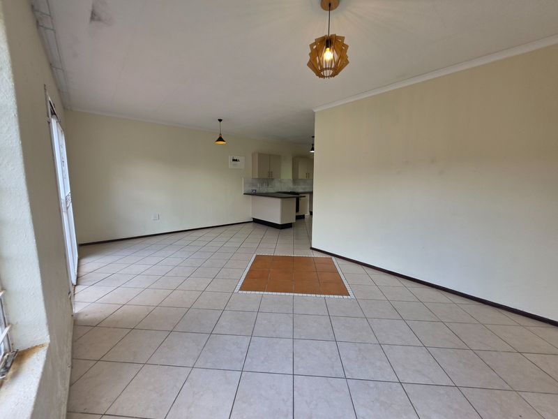 Spacious open-plan living and kitchen area featuring neutral tiled flooring, built-in cabinetry, and modern pendant lighting, offering a versatile layout for customization.