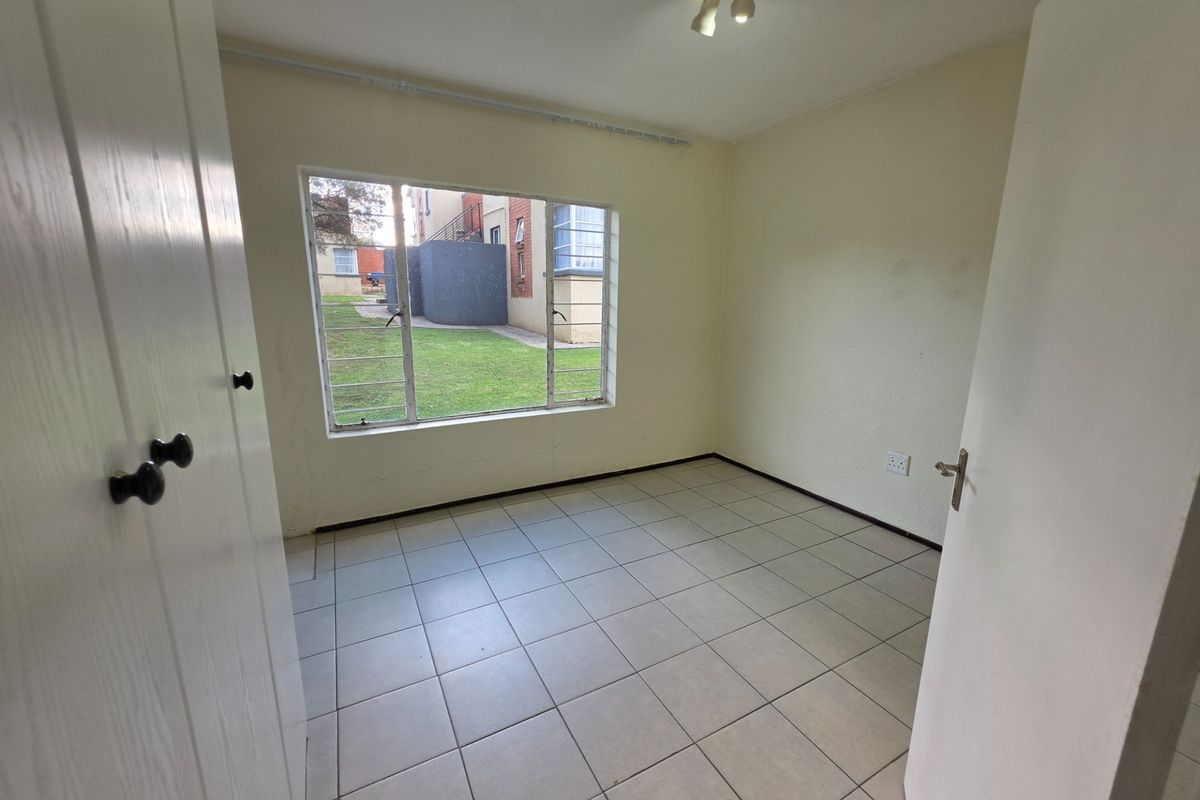 An empty bedroom featuring tiled flooring, a built-in cupboard, and a large window overlooking the exterior grounds.