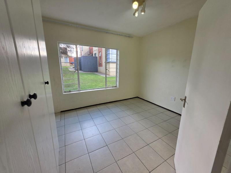 An empty bedroom featuring tiled flooring, a built-in cupboard, and a large window overlooking the exterior grounds.