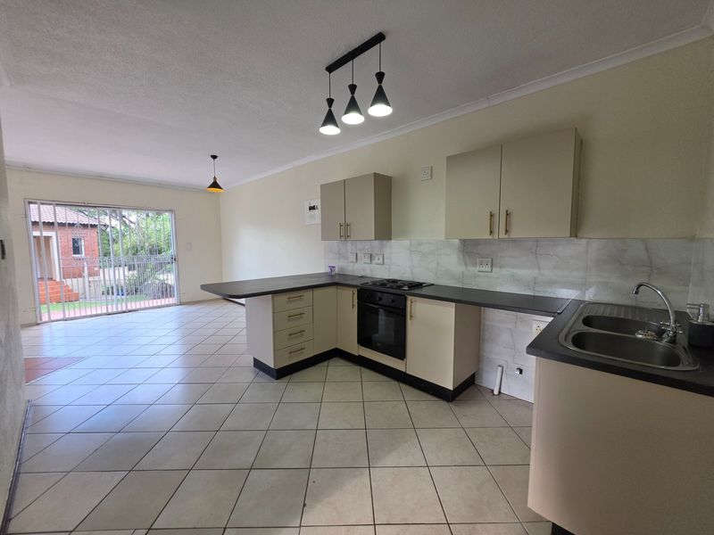 Spacious open-plan kitchen and living area featuring tiled floors, modern cabinetry, built-in appliances, and direct access to an outdoor patio through sliding glass doors.