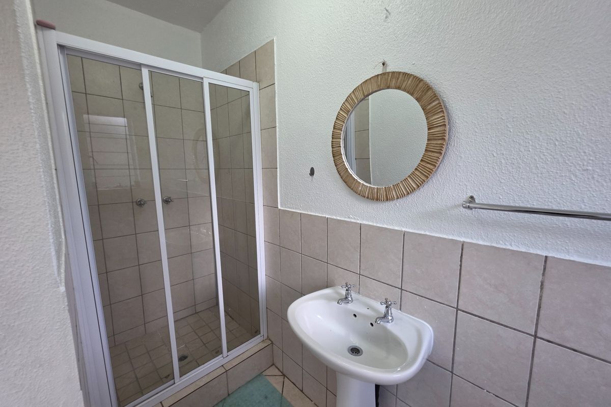 A functional bathroom featuring a pedestal basin, tiled splashback, and a glass-enclosed shower unit.