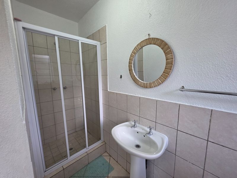 A functional bathroom featuring a pedestal basin, tiled splashback, and a glass-enclosed shower unit.