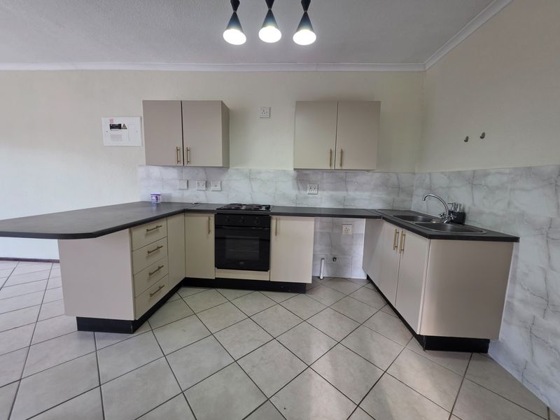 A functional kitchen featuring neutral cabinetry, dark countertops, a built-in oven with gas hob, and tiled flooring, offering a clean and practical workspace.