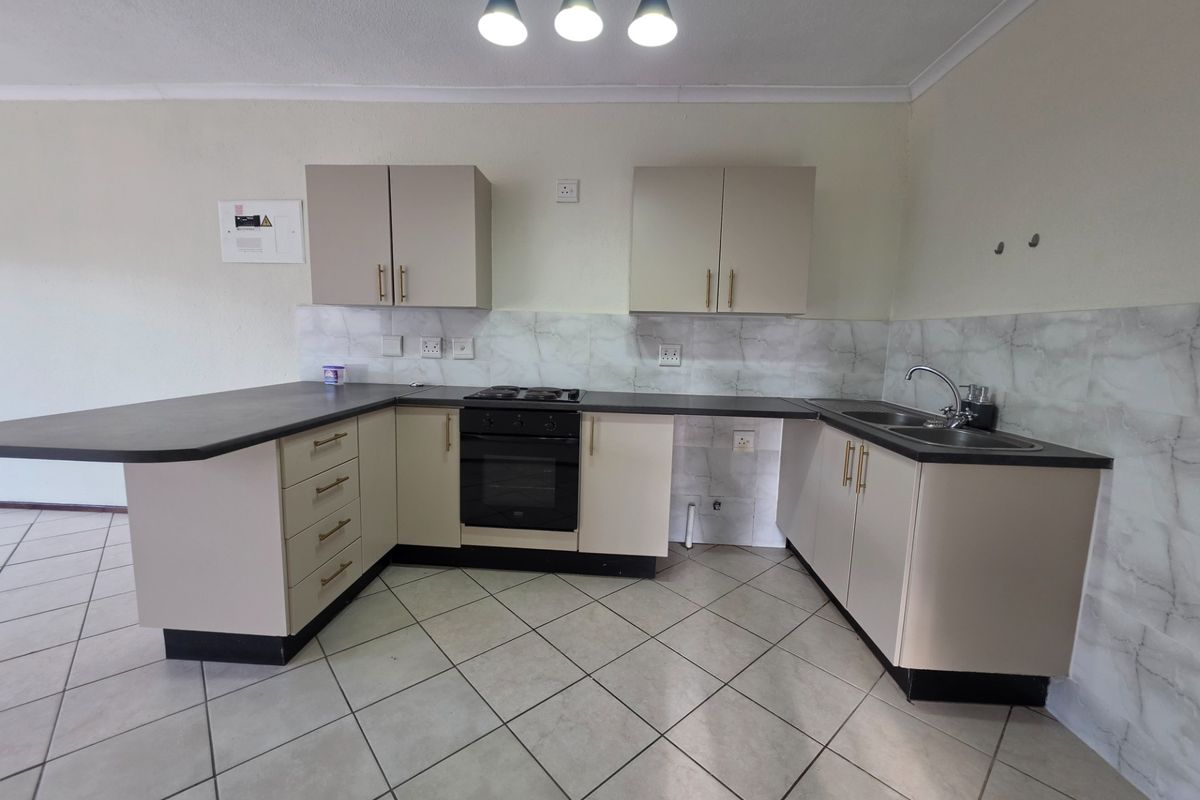 A functional kitchen featuring neutral cabinetry, dark countertops, a built-in oven with gas hob, and tiled flooring, offering a clean and practical workspace.