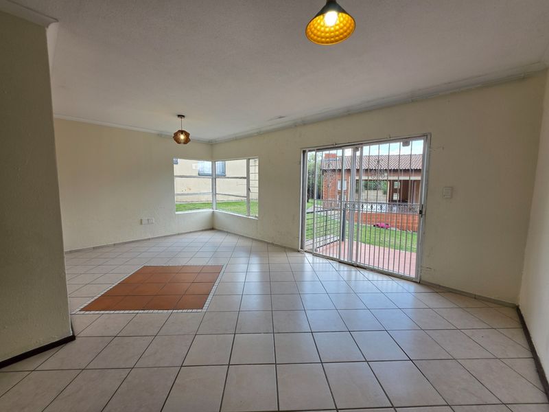 Spacious, empty living area featuring neutral tiled flooring, corner windows, and a sliding glass door with security gate leading to the exterior.