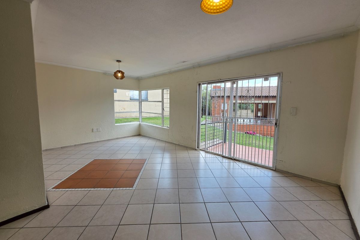 Spacious, empty living area featuring neutral tiled flooring, corner windows, and a sliding glass door with security gate leading to the exterior.