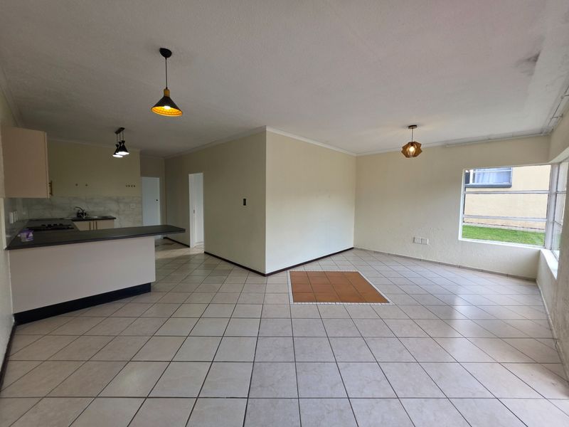 An open-plan living and kitchen area featuring tiled flooring, built-in cabinetry, a breakfast bar, and natural light from large windows.