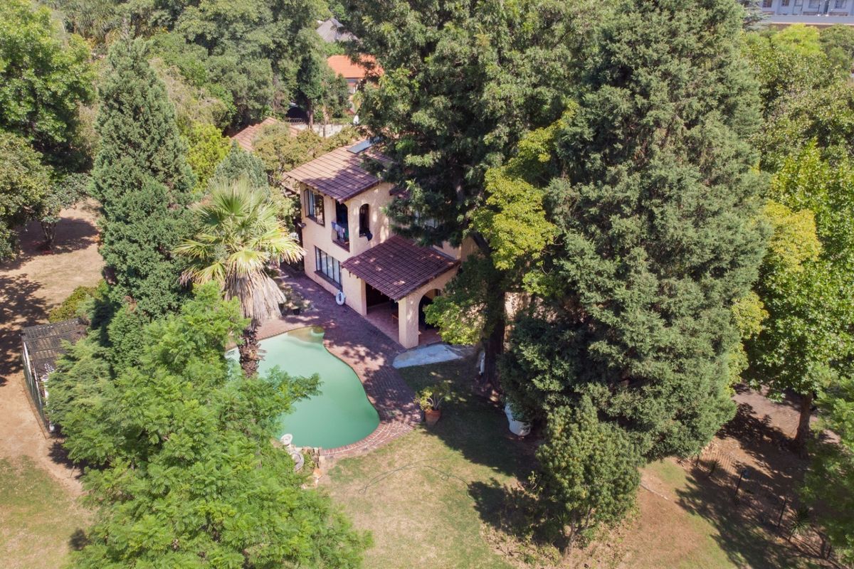 Aerial view of a residential property featuring a swimming pool, covered patio, and mature garden surroundings.