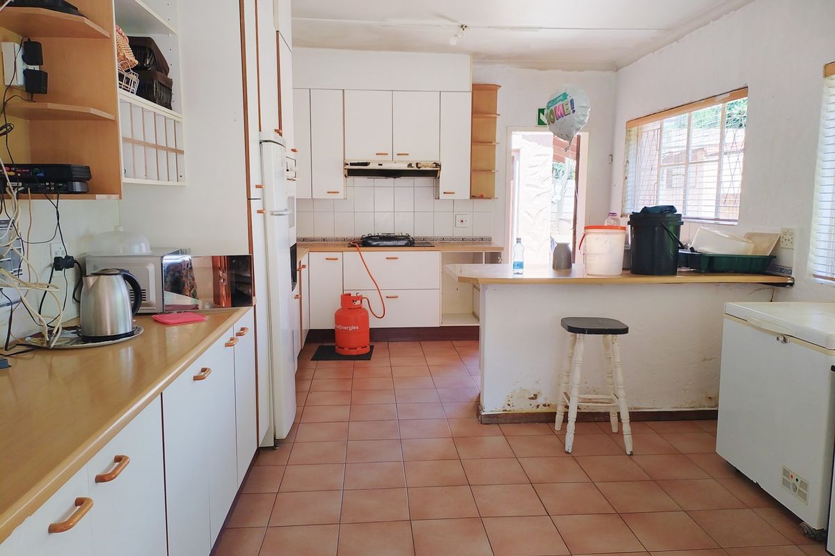 A dated kitchen featuring white built-in cabinetry, a gas hob, tiled flooring, and a breakfast counter, requiring cosmetic updates to modernize the space.