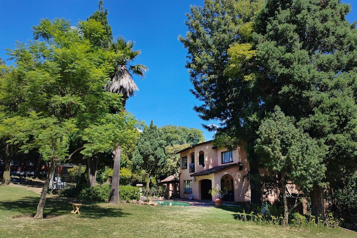 A view of the rear of the house featuring a swimming pool, established garden, and mature trees.