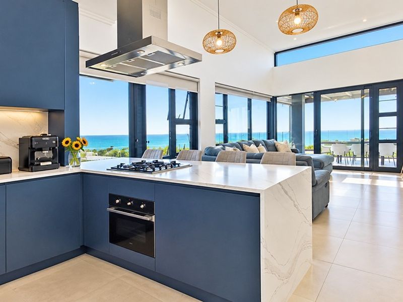 Modern open-plan kitchen and living area featuring high-end finishes, a large island, and expansive floor-to-ceiling windows with panoramic ocean views.