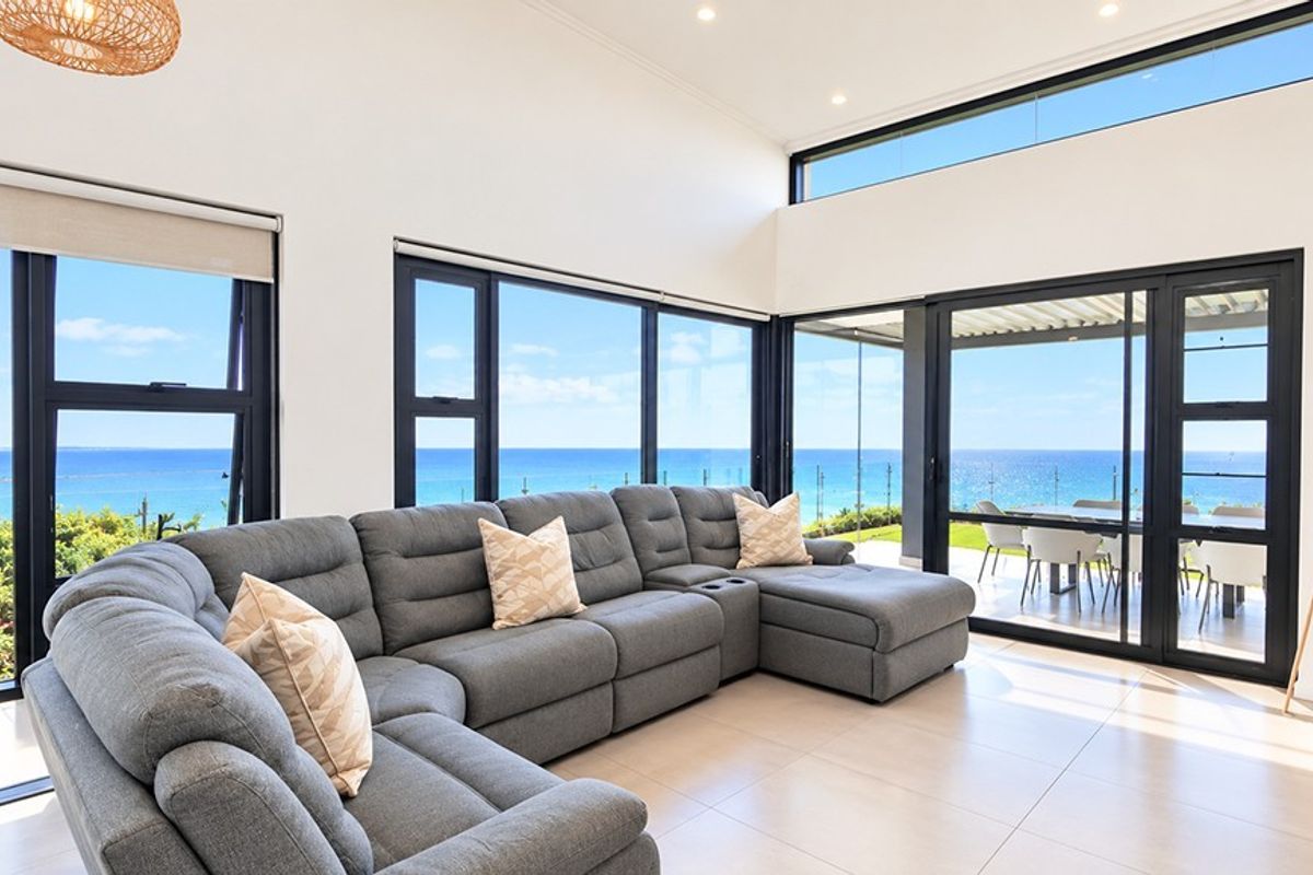 Spacious living area featuring large format floor tiles, expansive black aluminium sliding doors, and clerestory windows offering panoramic ocean views.