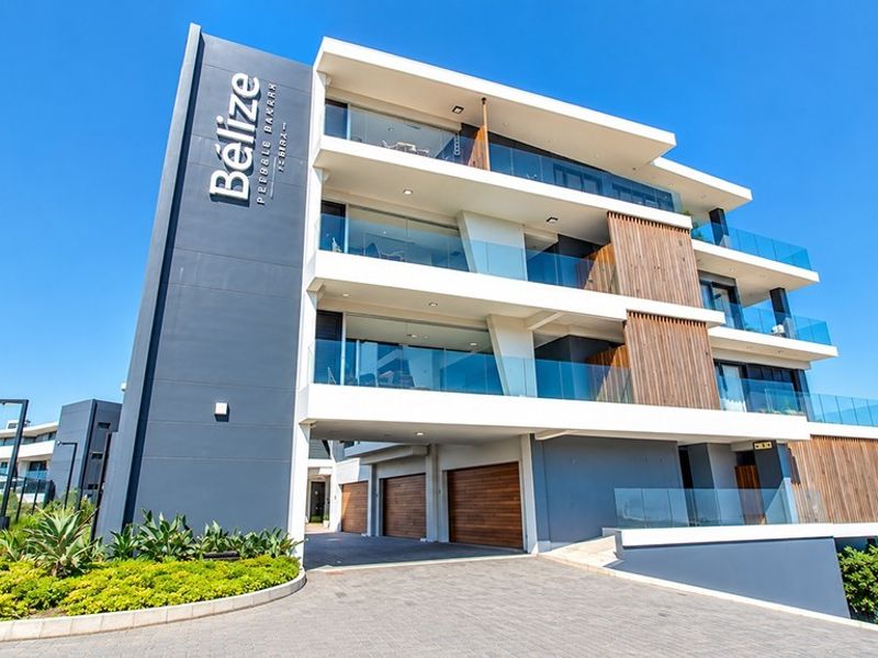 Modern multi-story penthouse building featuring contemporary architectural design, glass balconies, timber accents, and a paved driveway entrance.