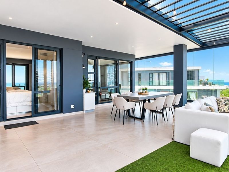 Spacious covered balcony featuring a louvered pergola, tiled flooring, and glass sliding doors, offering seamless indoor-outdoor flow with panoramic coastal views.