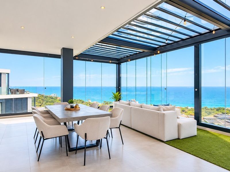 Spacious enclosed balcony featuring floor-to-ceiling glass walls, panoramic ocean views, tiled flooring, and a modern retractable roof system.