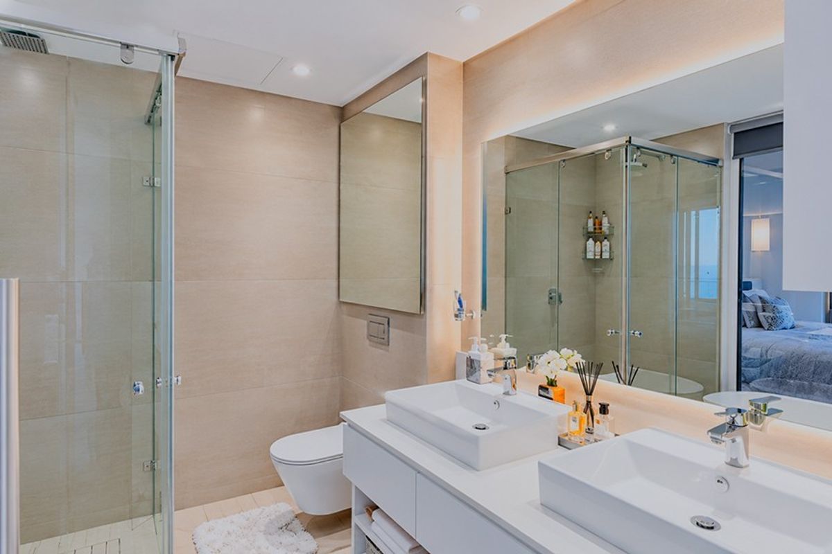 Modern bathroom featuring a double vanity with vessel sinks, a wall-mounted toilet, and a spacious glass-enclosed shower with neutral tiling.