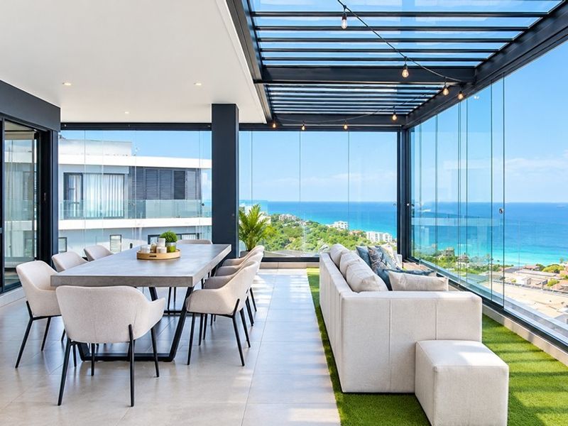 A luxurious enclosed balcony featuring a glass roof, frameless sliding doors, and panoramic ocean views, perfect for year-round indoor-outdoor entertaining.