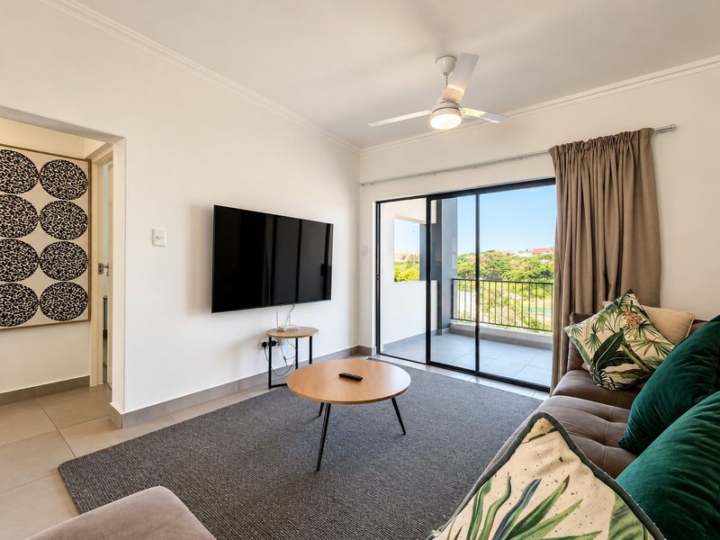 Bright living room featuring tiled flooring, a ceiling fan, and large sliding glass doors providing access to a private balcony.