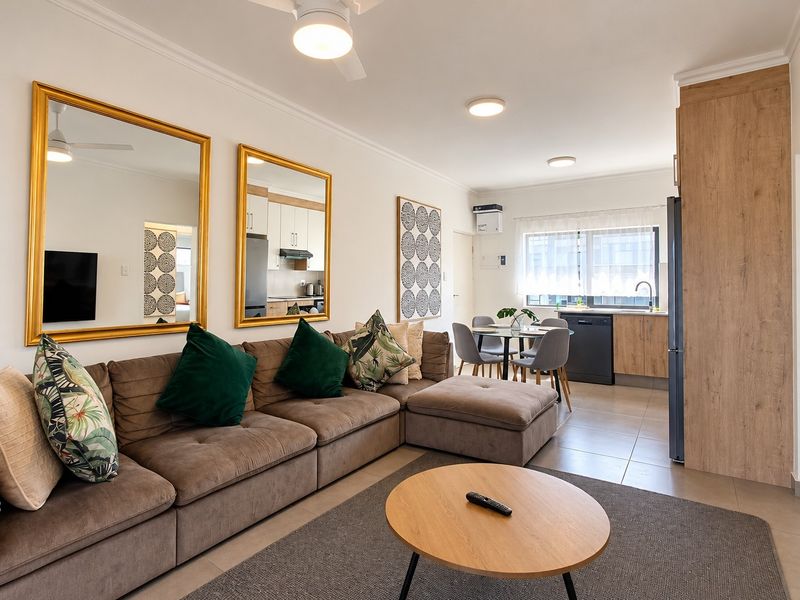 A bright open-plan living and dining area featuring tiled floors, modern kitchen cabinetry, and integrated lighting, creating a functional and cohesive living space.
