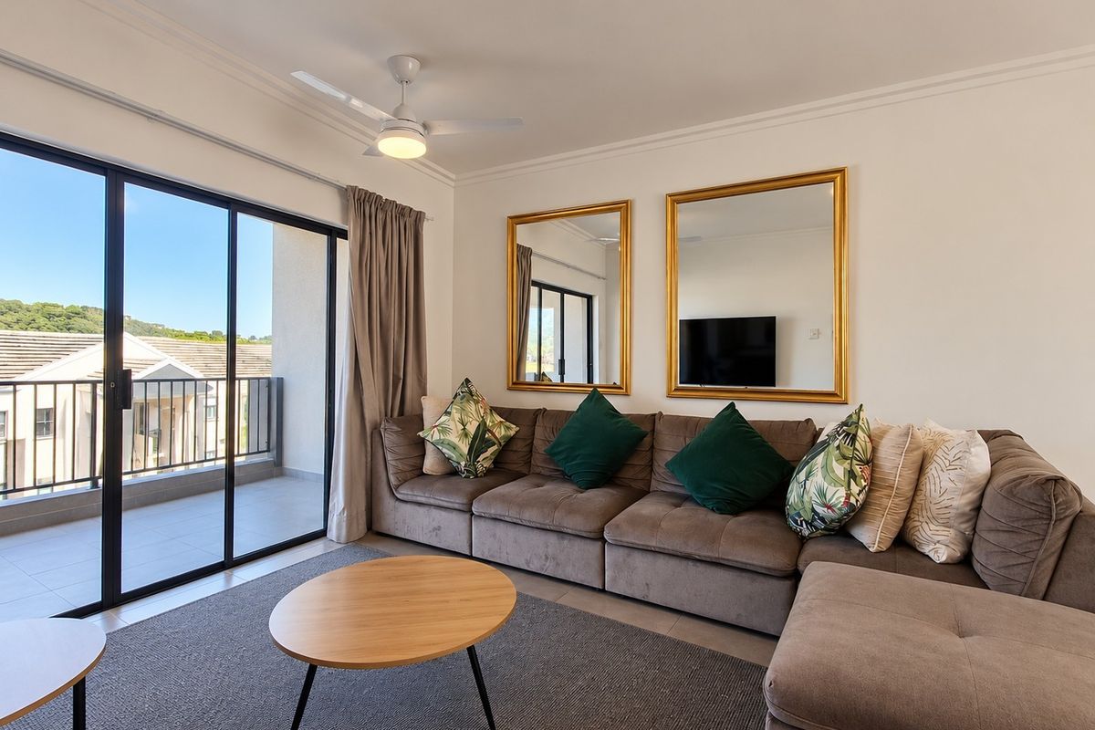 A bright living room featuring a ceiling fan, cove molding, and large sliding glass doors that open onto a private balcony.