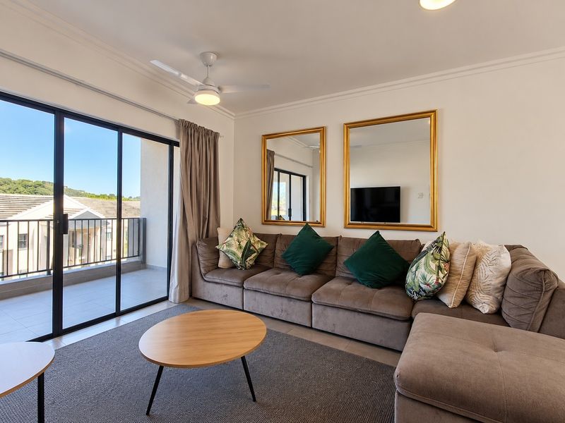 A bright living room featuring a ceiling fan, cove molding, and large sliding glass doors that open onto a private balcony.