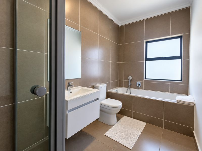 Modern bathroom featuring a wall-mounted vanity, bathtub with shower mixer, and neutral floor-to-ceiling tiling.