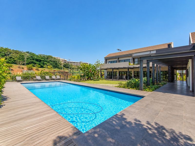 A well-maintained swimming pool area featuring timber decking, a tiled patio with a pergola, and landscaped garden surroundings.