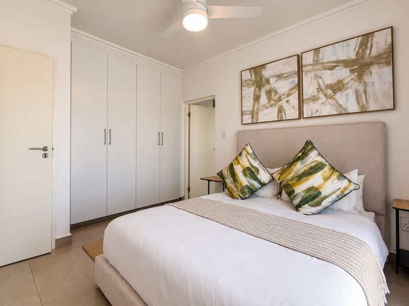 A well-maintained bedroom featuring built-in cupboards, tiled flooring, and a modern ceiling fan, offering a clean and functional living space.