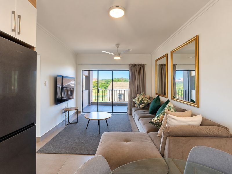 Bright open-plan living area featuring tiled floors, a ceiling fan, and large sliding glass doors that provide seamless access to the balcony.