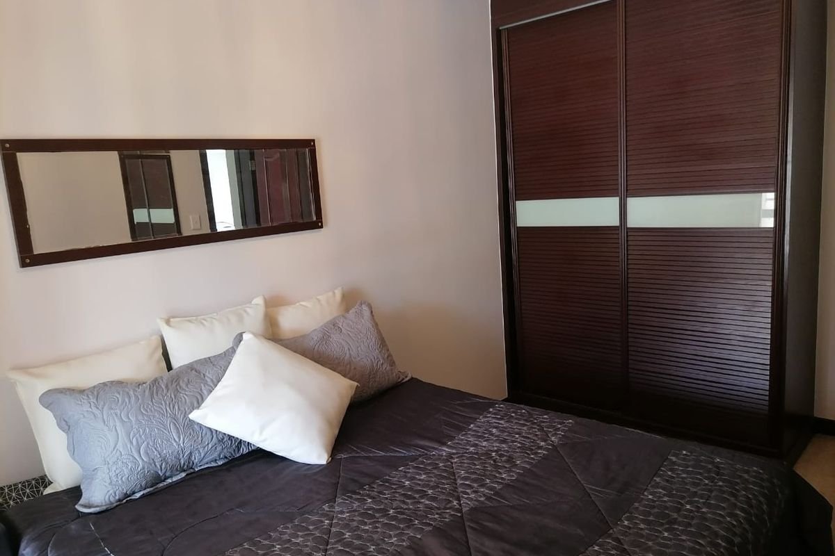 A well-maintained bedroom featuring a large, dark wood built-in sliding door wardrobe and neutral wall finishes.
