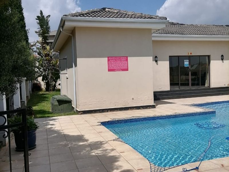 Outdoor pool area featuring a tiled deck, swimming pool with safety net, and access to the main building via sliding glass doors.