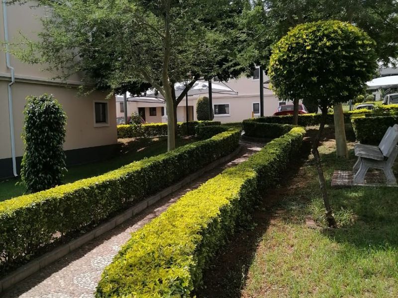 A well-maintained communal garden area featuring manicured hedges, a pebble pathway, and mature trees within the apartment complex grounds.