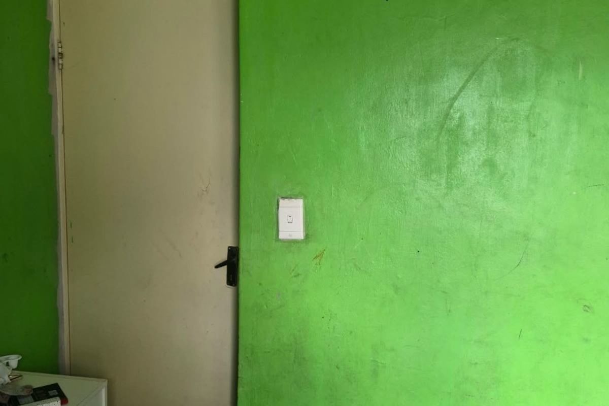 A bedroom interior featuring bright green painted walls with visible scuff marks and exposed electrical wiring above a standard internal door.