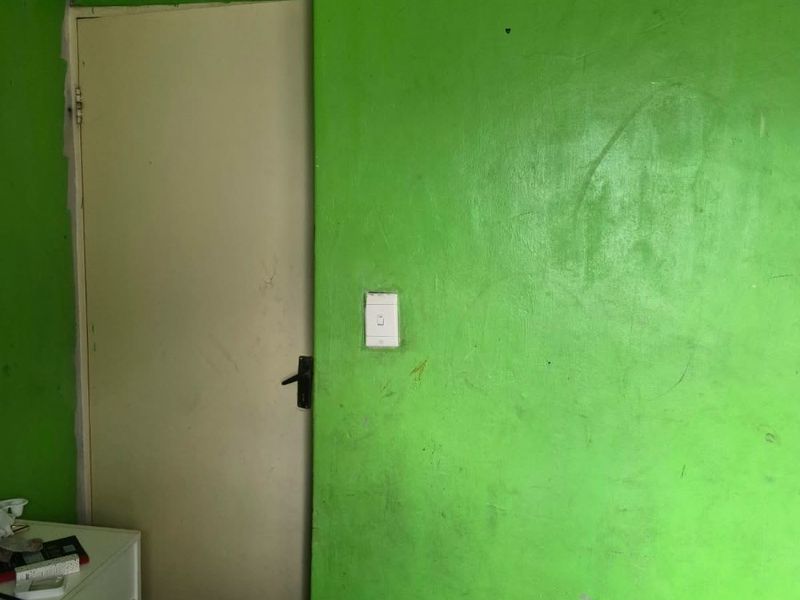 A bedroom interior featuring bright green painted walls with visible scuff marks and exposed electrical wiring above a standard internal door.