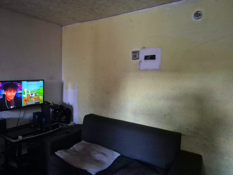 A living room area featuring a wall-mounted security keypad and electrical distribution board, currently requiring cosmetic updates to the wall finishes.