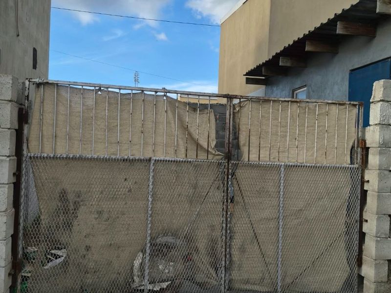 Front entrance featuring a metal security gate mounted between concrete block pillars, showing significant signs of wear and weathering.