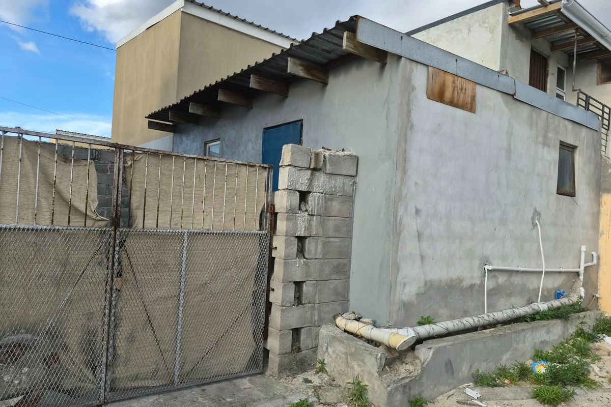 Rear exterior view of the property showing unfinished concrete block walls, corrugated metal roofing, and external plumbing infrastructure.
