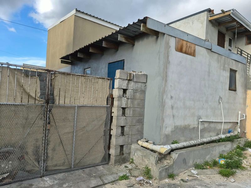 Rear exterior view of the property showing unfinished concrete block walls, corrugated metal roofing, and external plumbing infrastructure.