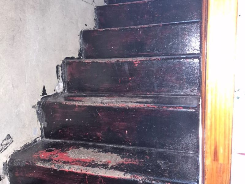 A staircase featuring a wooden handrail, currently showing significant wear and paint deterioration on the treads, requiring refurbishment.