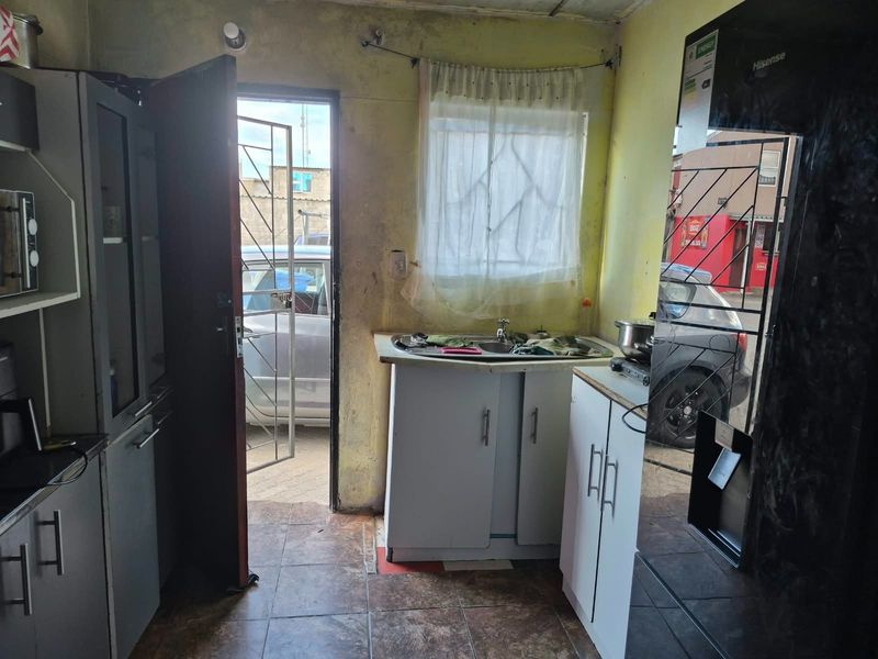 A compact kitchen area featuring basic cabinetry, a sink, and tiled flooring, with direct access to the exterior through a security gate.