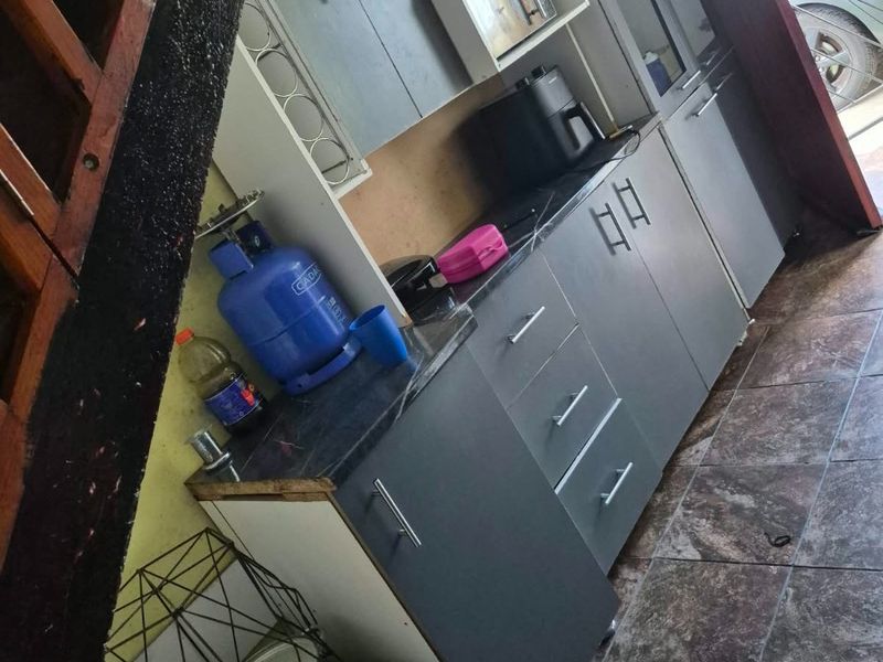 Compact kitchen area featuring grey built-in cabinetry, dark laminate countertops, and tiled flooring, with direct access to an exterior security gate.