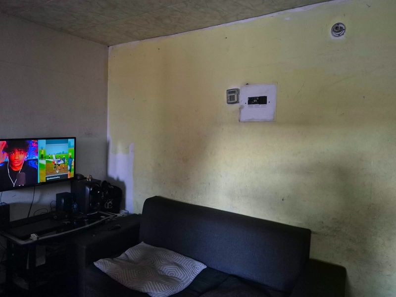 A living room area featuring an alarm keypad and electrical distribution board, currently showing significant wall surface wear and discoloration.